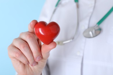 Photo of Doctor with red heart on light blue background, closeup