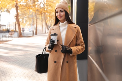 Photo of Beautiful young woman with cup of coffee on city street. Autumn walk