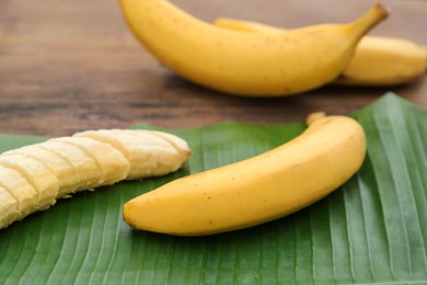 Photo of Delicious ripe bananas and fresh leaf on wooden table