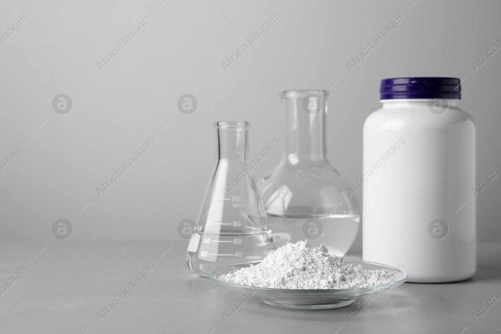 Photo of Plate with calcium carbonate powder, jar and laboratory glassware on grey table. Space for text