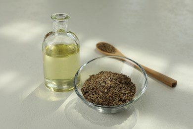 Photo of Caraway (Persian cumin) seeds in bowl and essential oil on white table