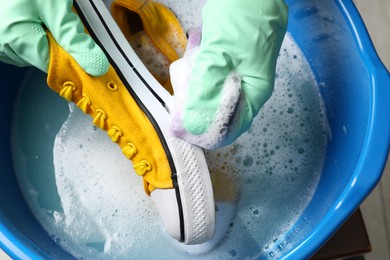 Photo of Woman with gloves and sponge cleaning stylish sneakers in wash basin, top view