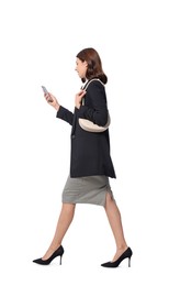 Happy young woman in formal suit using smartphone while walking on white background