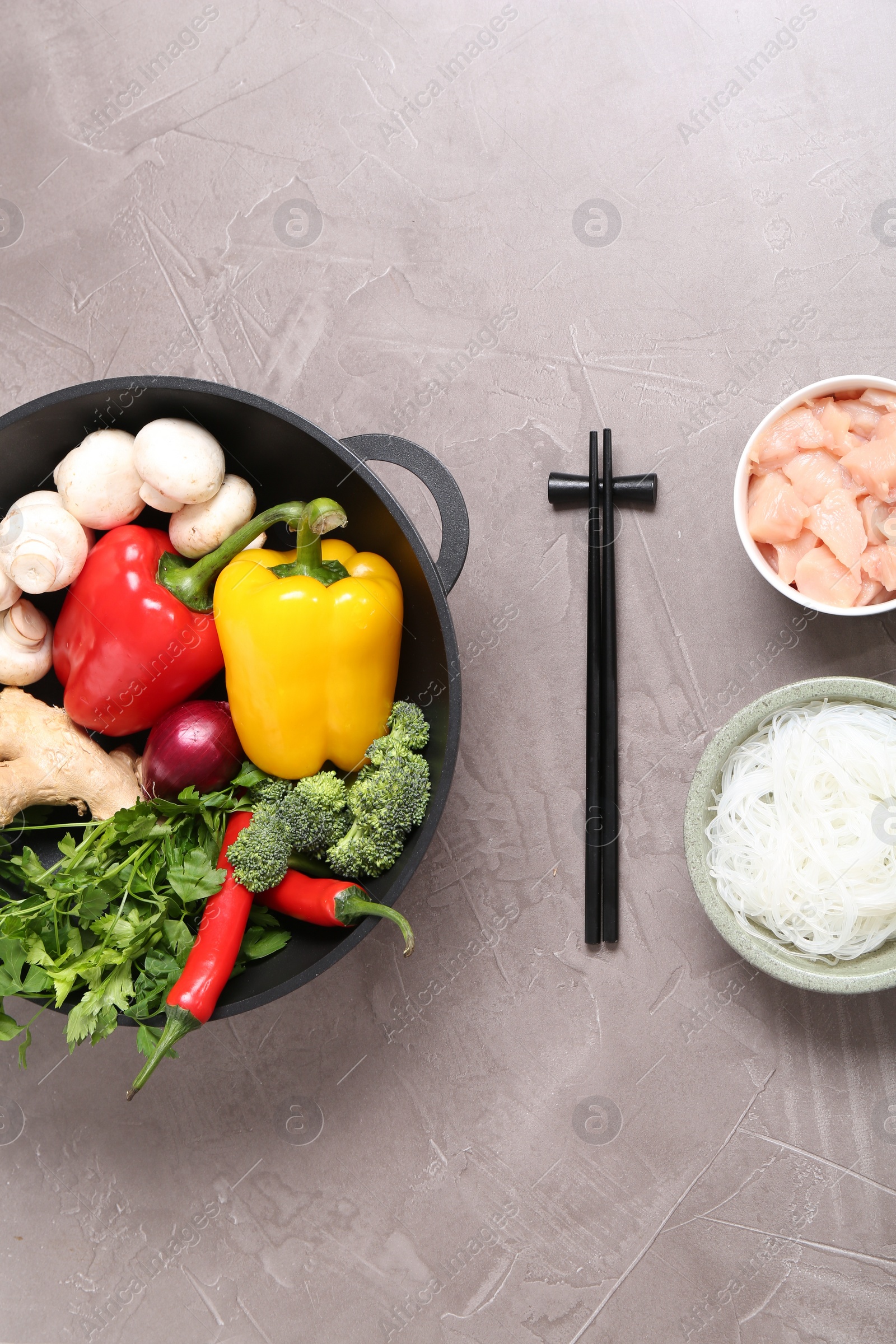 Photo of Wok, chopsticks and different products on grey textured table, flat lay