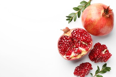 Photo of Fresh pomegranates and green leaves on white background, flat lay. Space for text
