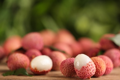 Photo of Pile of fresh ripe lychees on wooden table outdoors, space for text