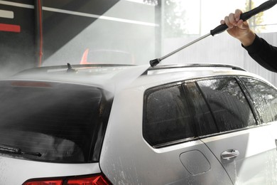 Man washing auto with high pressure water jet at outdoor car wash, closeup