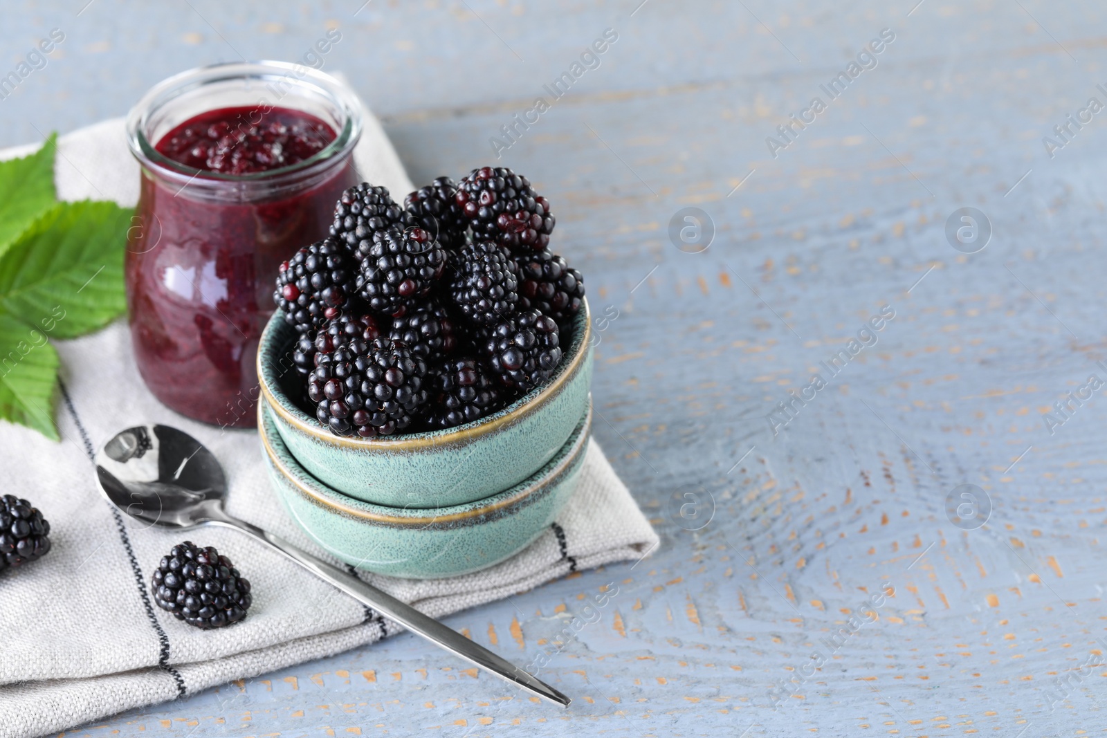 Photo of Fresh ripe blackberries and tasty jam on light grey wooden table. Space for text