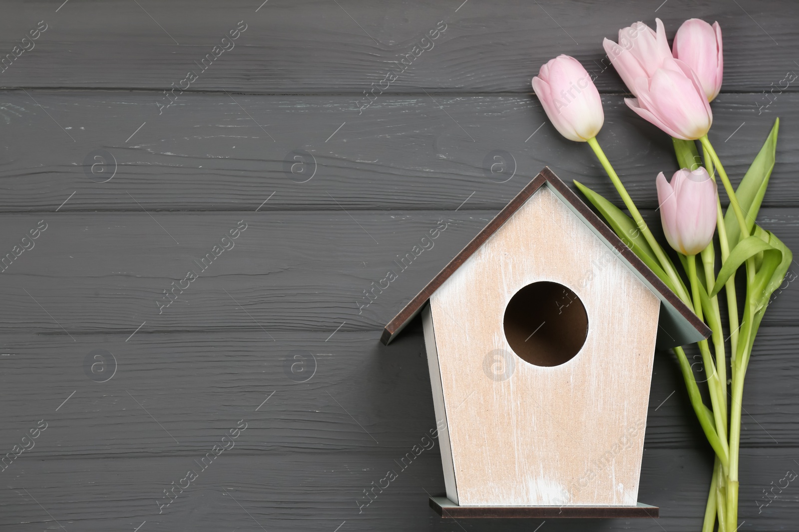 Photo of Beautiful bird house and pink tulips on grey wooden table, flat lay. Space for text