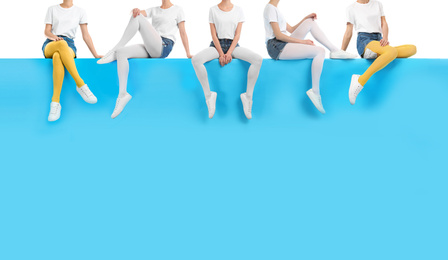 Women wearing different tights and stylish shoes sitting on color background, closeup 