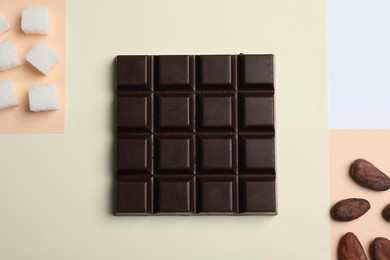 Delicious dark chocolate bar, refined sugar and cocoa beans on color background, flat lay