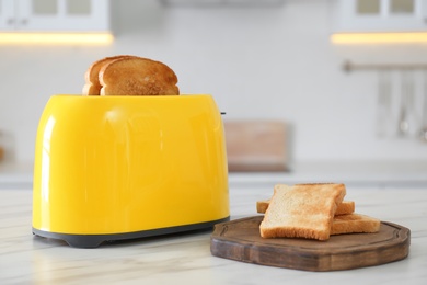 Modern toaster and bread slices on white marble table in kitchen