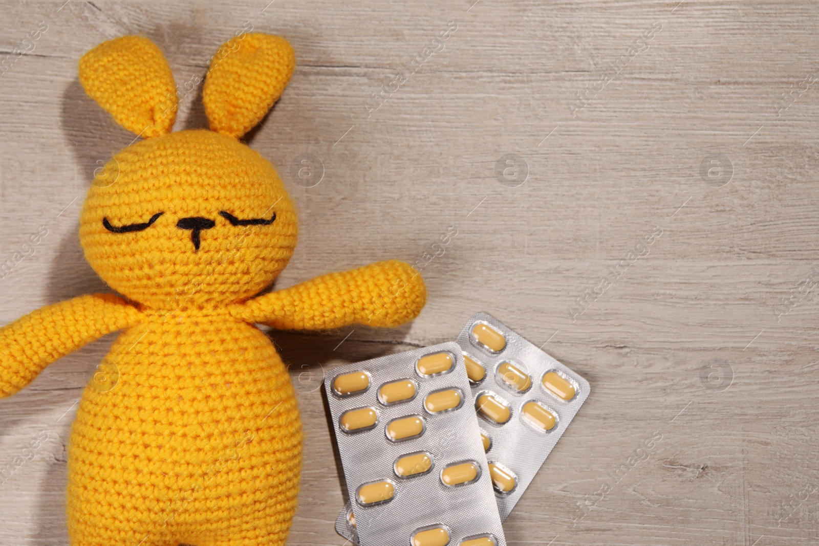 Photo of Toy bunny and pills on wooden background, flat lay. Space for text