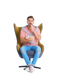 Photo of Handsome young man with bowl of popcorn in armchair on white background. Watching cinema