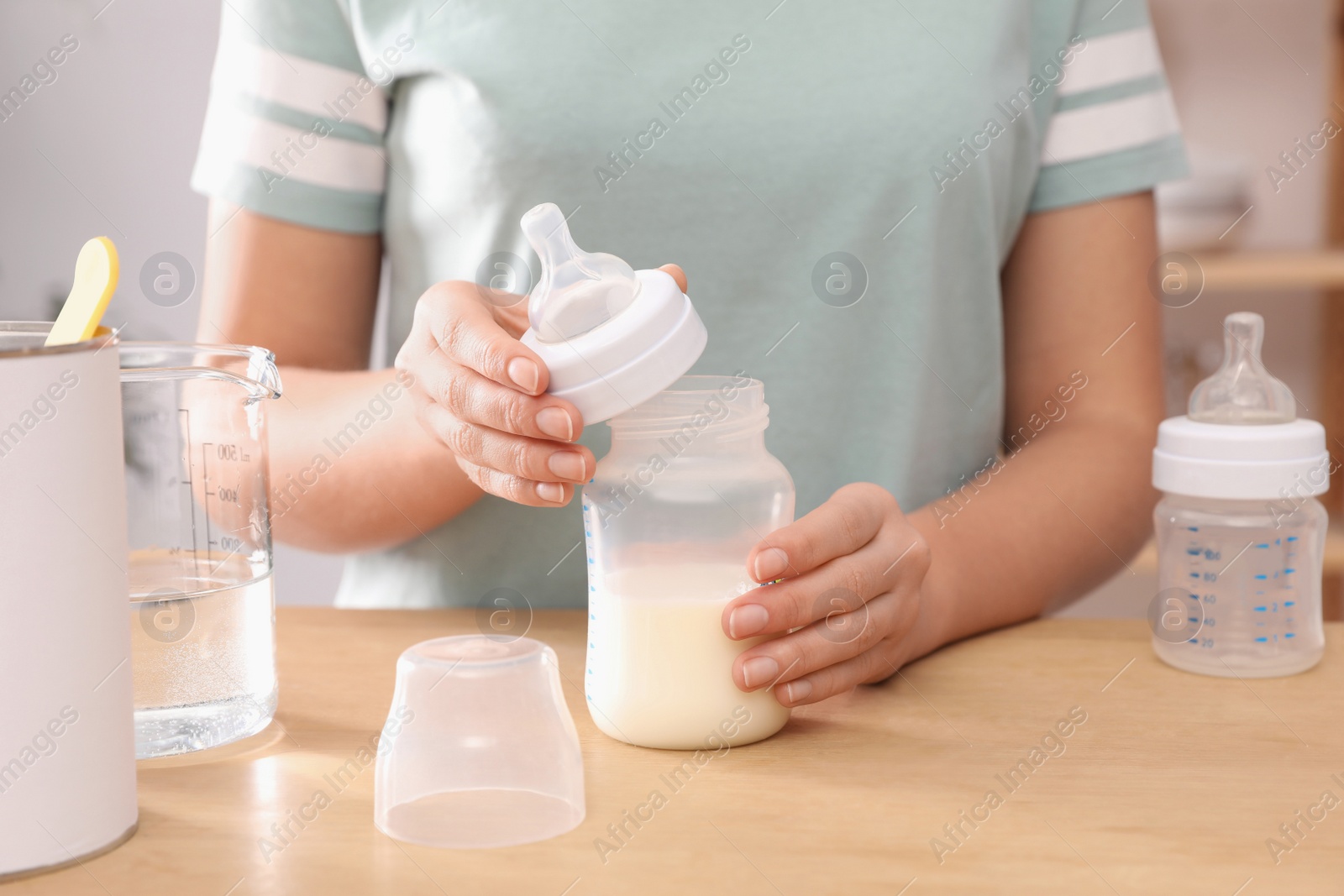 Photo of Woman preparing infant formula at table indoors, closeup. Baby milk