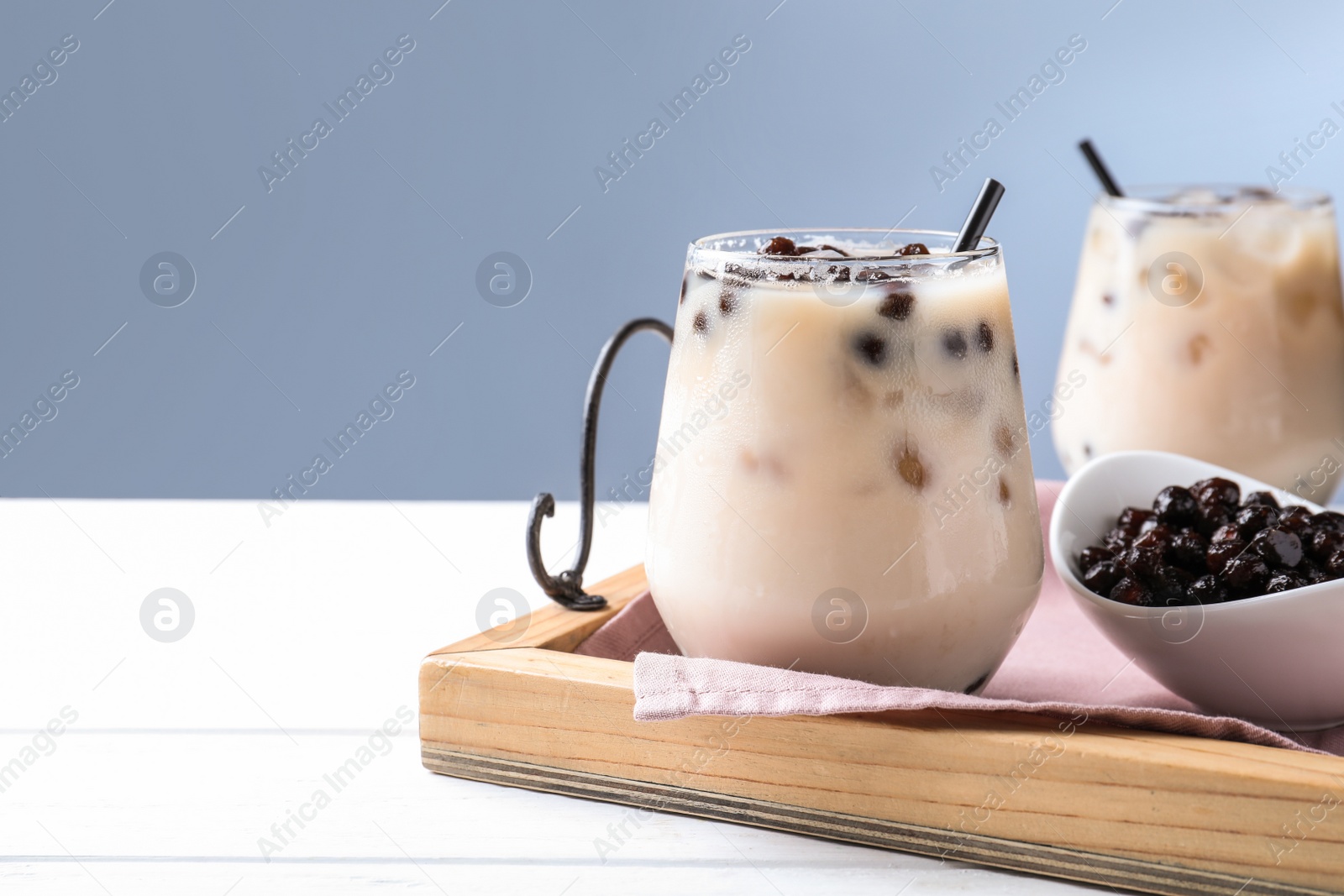 Photo of Bubble milk tea with tapioca balls on white wooden table against blue background. Space for text