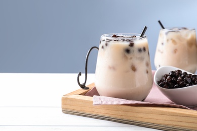 Photo of Bubble milk tea with tapioca balls on white wooden table against blue background. Space for text