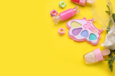 Photo of Decorative cosmetics for kids. Eye shadow palette, lipsticks, accessories and flowers on yellow background, closeup. Space for text