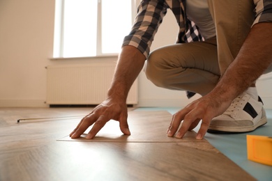Photo of Professional worker installing new parquet flooring indoors, closeup