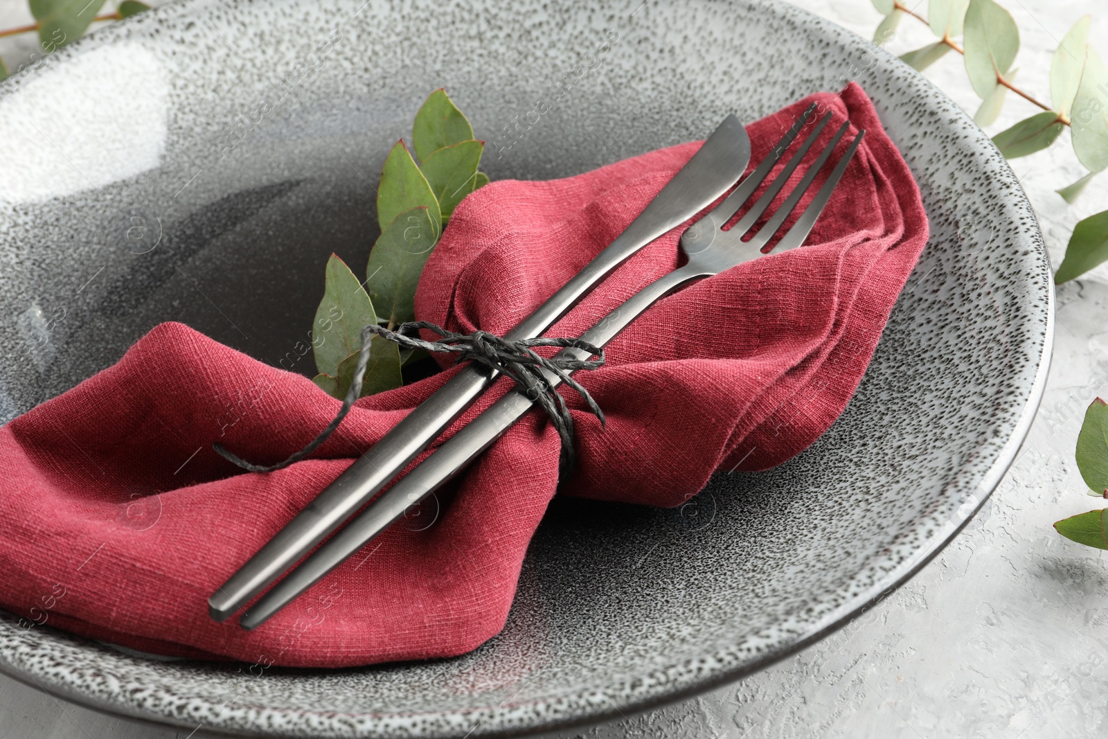 Photo of Stylish setting with cutlery, napkin, eucalyptus branches and plate on grey textured table, closeup