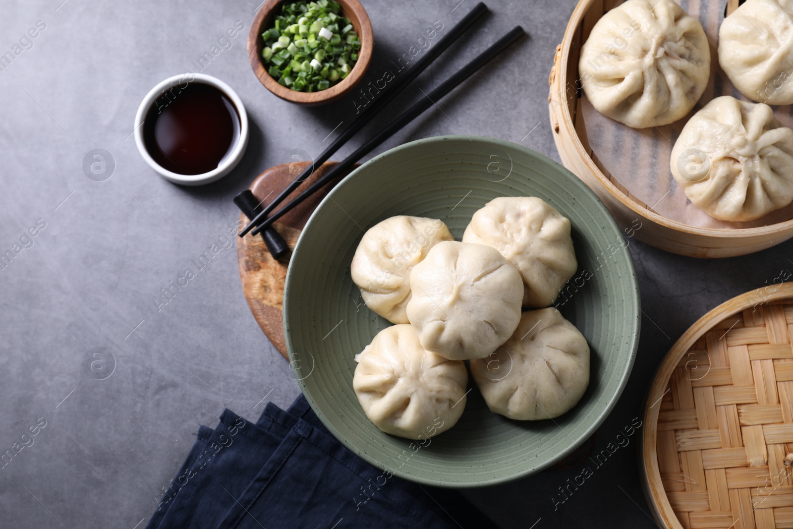 Photo of Delicious bao buns (baozi), chopsticks, soy sauce and green onion on grey table, flat lay