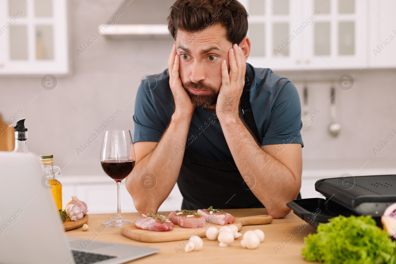 Photo of Man making dinner while watching online cooking course via laptop in kitchen