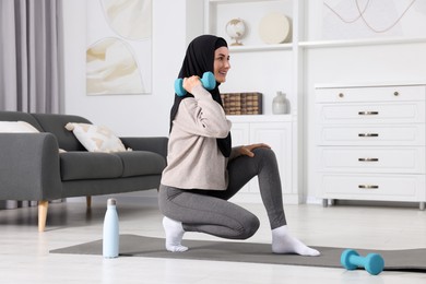 Photo of Muslim woman in hijab doing exercise on fitness mat at home
