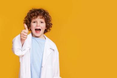 Photo of Little boy in medical uniform showing thumb up on yellow background. Space for text