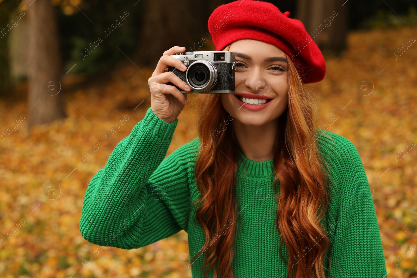 Photo of Smiling woman with camera taking photo in autumn park