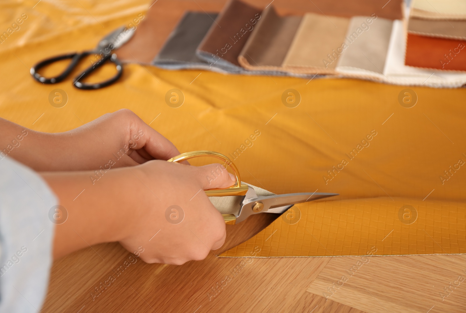 Photo of Woman cutting orange leather with scissors at wooden table, closeup