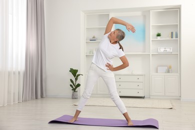 Senior woman practicing yoga on mat at home