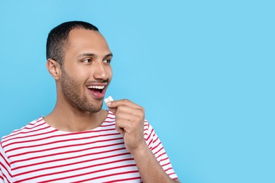 Photo of Happy young man with bubble gums on light blue background. Space for text