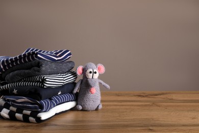 Stack of baby boy's clothes and toy on wooden table against brown background, space for text