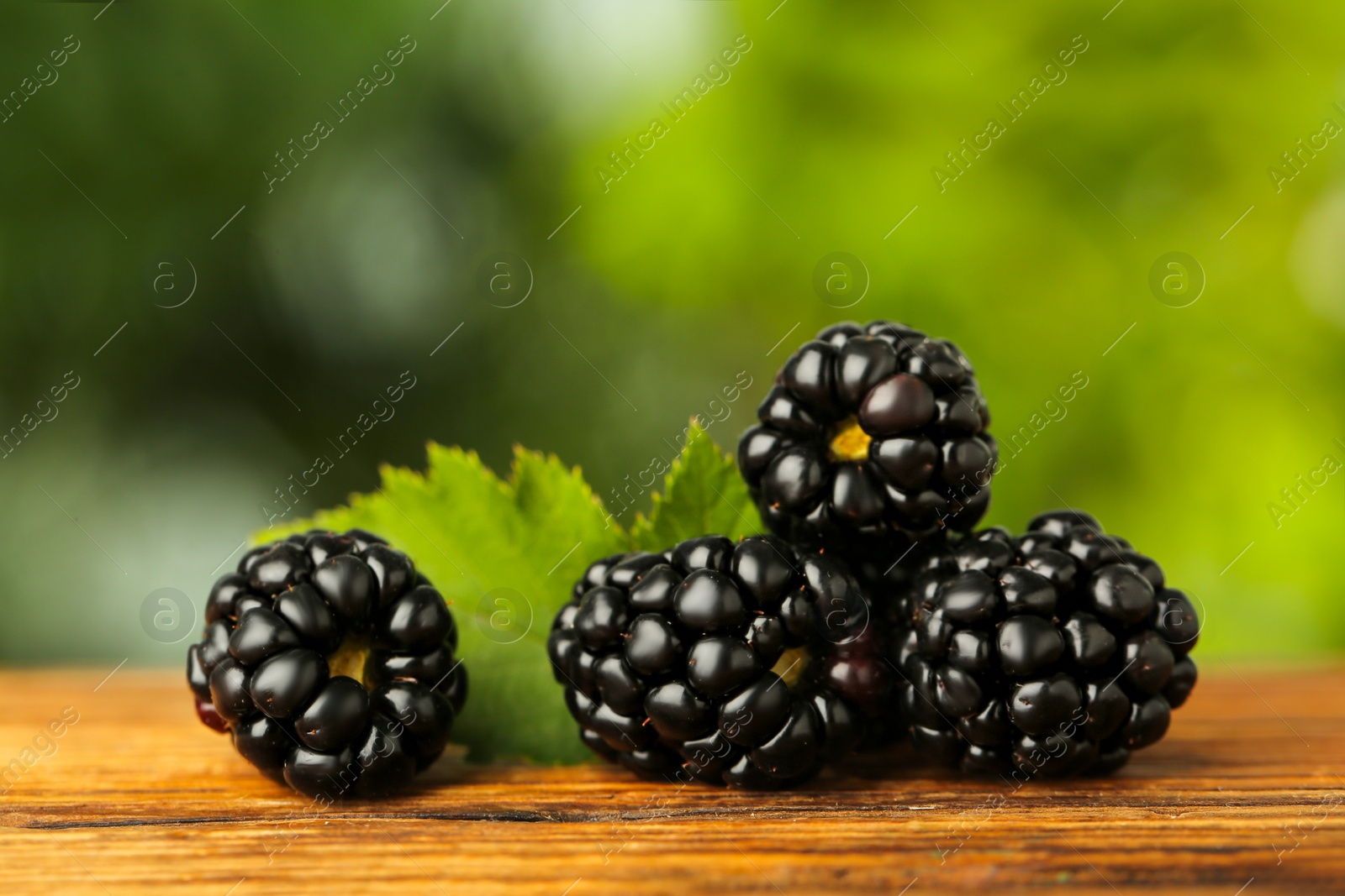 Photo of Fresh ripe blackberries on wooden table outdoors, closeup