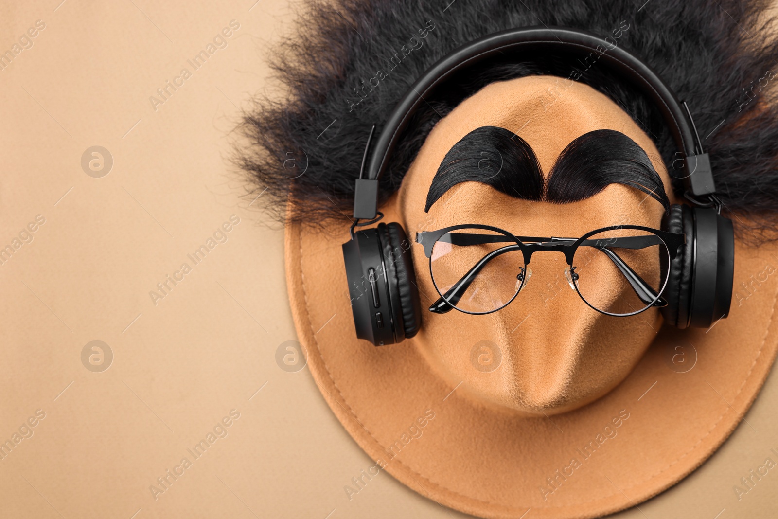 Photo of Man's face made of artificial hair, eyebrows, glasses and hat on beige background, top view. Space for text