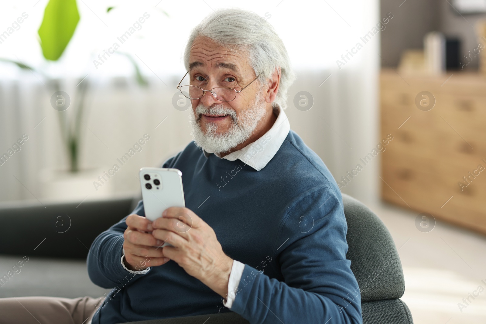 Photo of Portrait of happy grandpa with glasses using smartphone indoors