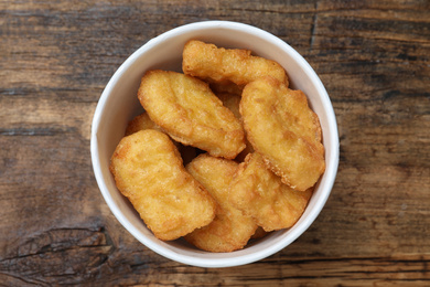 Photo of Bucket with tasty chicken nuggets on wooden table, top view