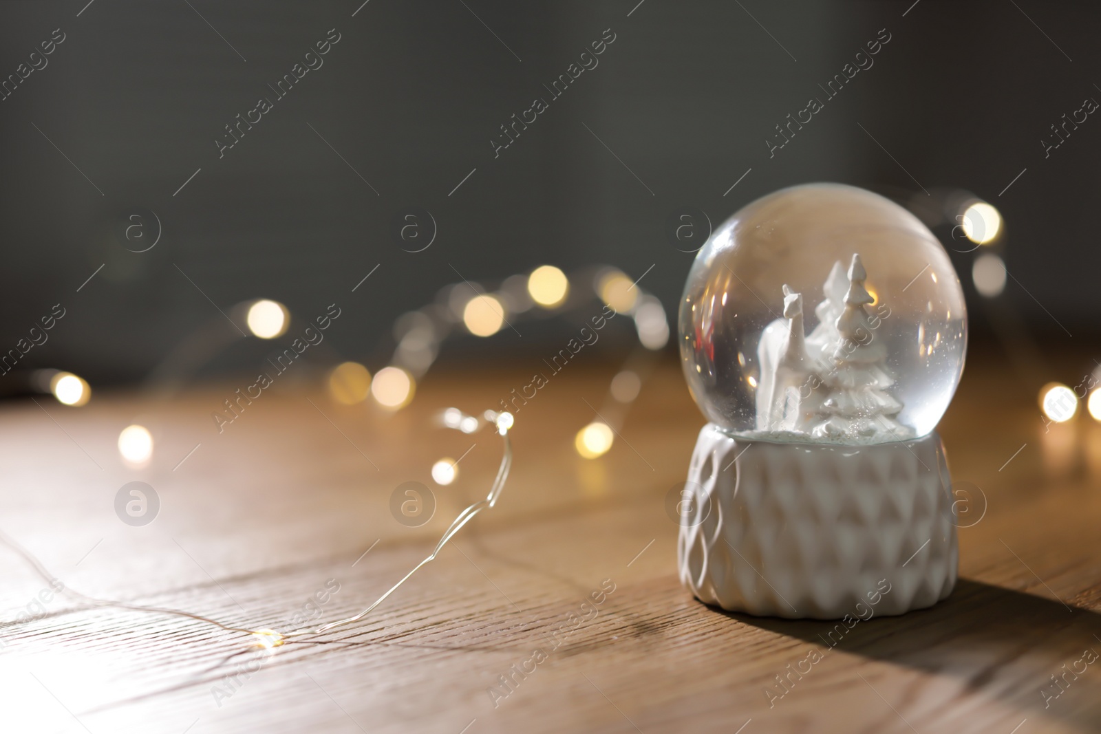 Photo of Snow globe with Christmas lights on wooden table. Space for text