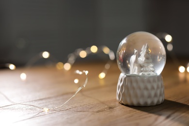 Snow globe with Christmas lights on wooden table. Space for text