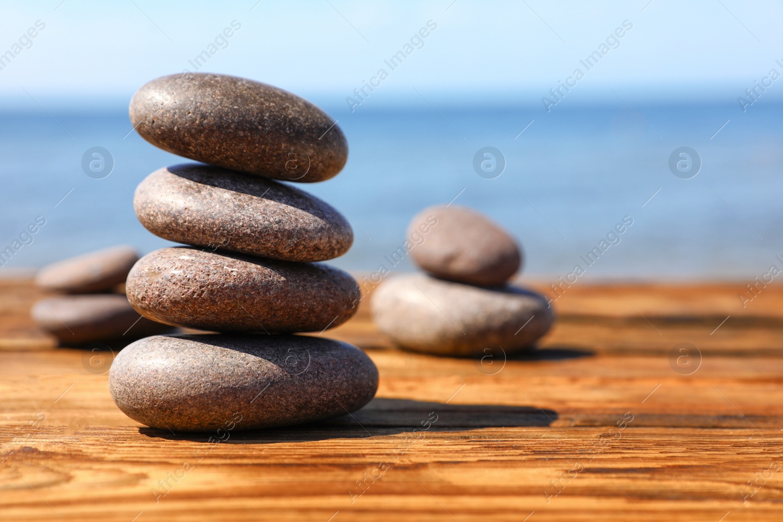 Photo of Stack of stones on wooden table against seascape, space for text. Zen concept