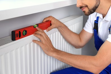 Professional plumber using bubble level for installing new heating radiator indoors, closeup