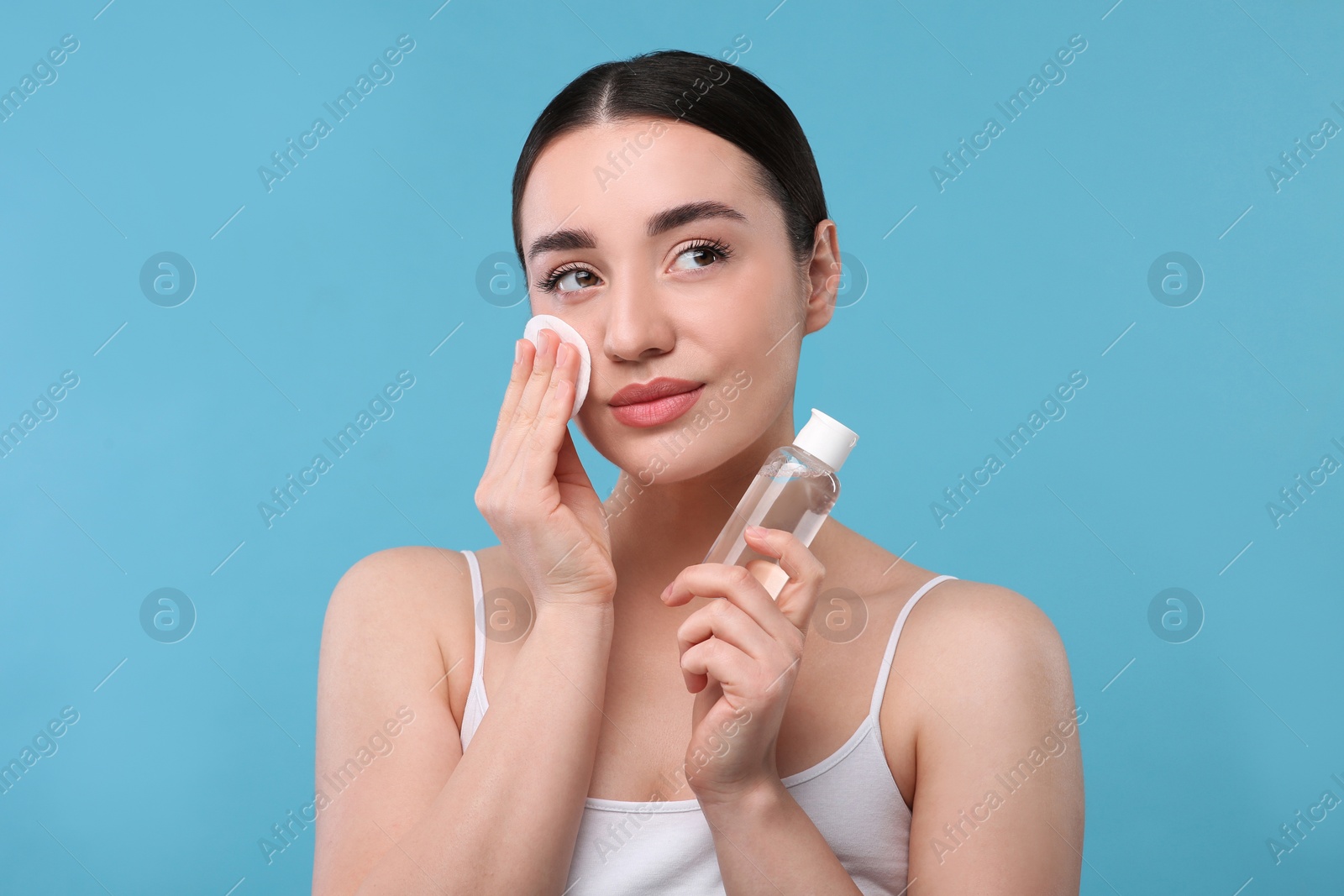 Photo of Beautiful woman removing makeup with cotton pad on light blue background