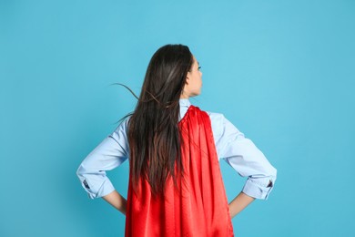 Photo of Young woman wearing superhero cape on light blue background, back view