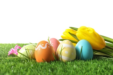 Photo of Colorful painted Easter eggs and flowers on green grass against white background