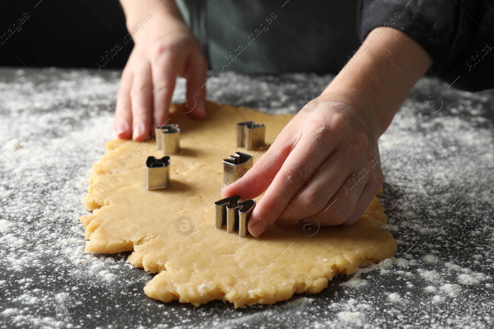 Photo of Shortcrust pastry. Woman making cookies with cutters at grey table, closeup