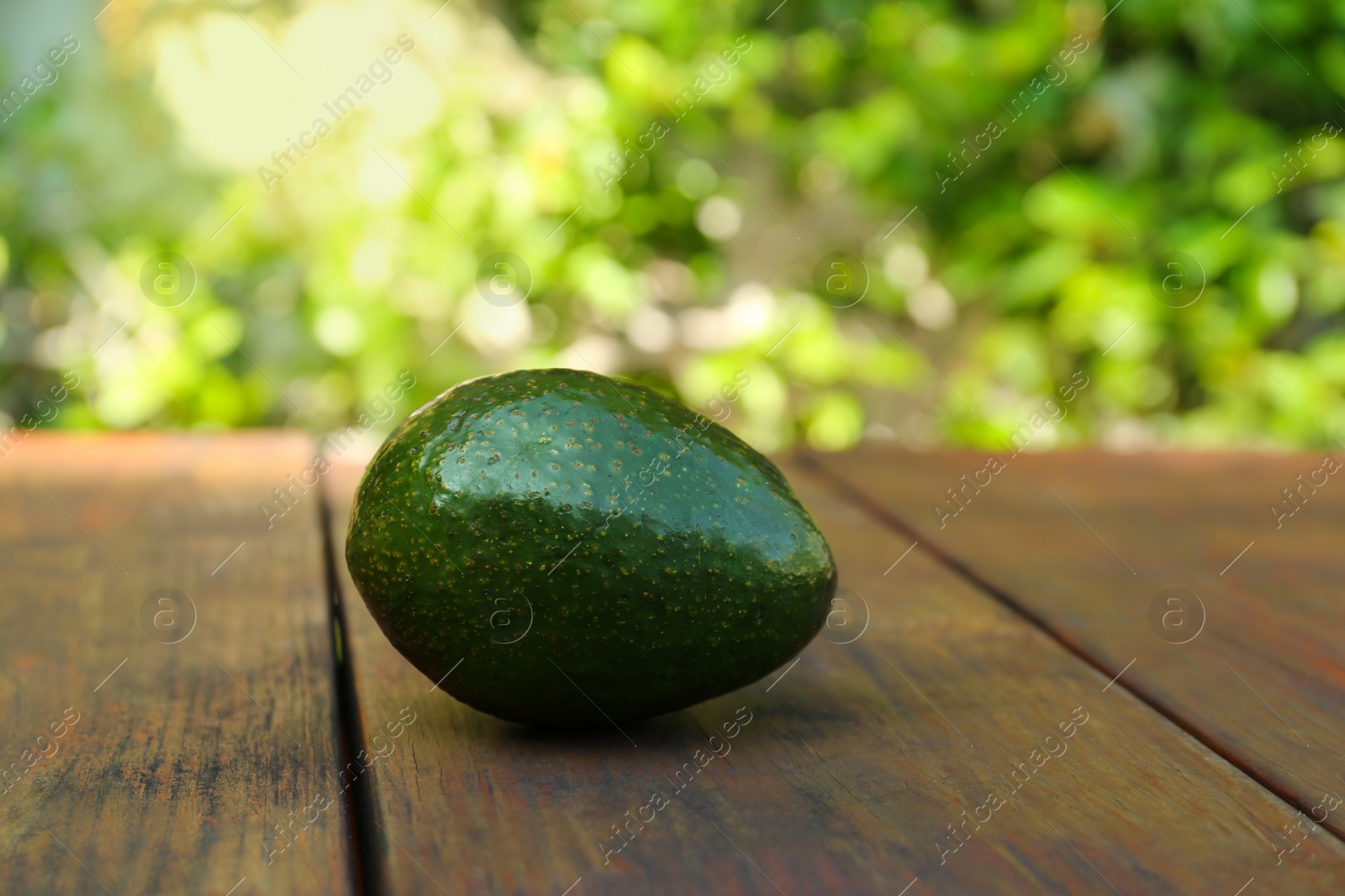 Photo of Fresh whole avocado on wooden table outdoors. Space for text