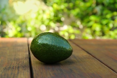 Photo of Fresh whole avocado on wooden table outdoors. Space for text