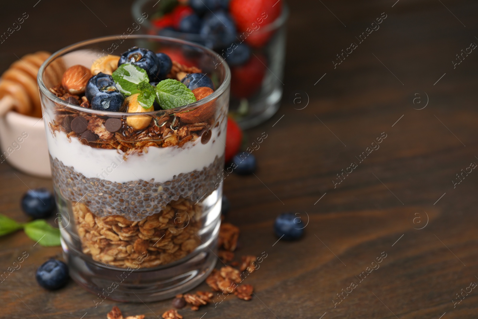 Photo of Tasty granola with berries, nuts, yogurt and chia seeds in glass on wooden table, closeup. Space for text