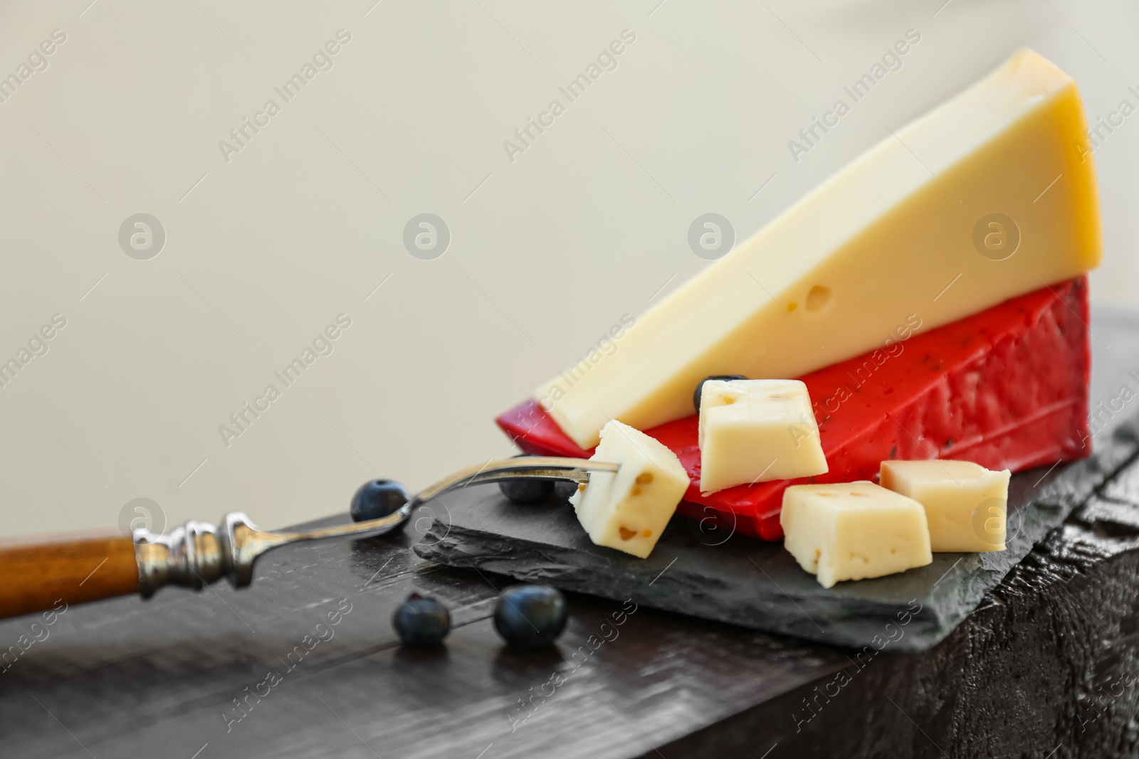 Photo of Different delicious cheeses, fork and blueberries on slate plate, closeup