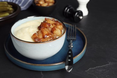 Photo of Potato puree and tasty fried cracklings on black table, space for text. Cooked pork lard